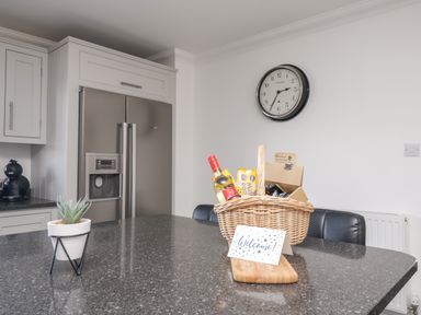 A kitchen with a gray countertop island featuring a small plant and a wicker basket with snacks and a welcome card at Mill End in Eamont Bridge near Penrith