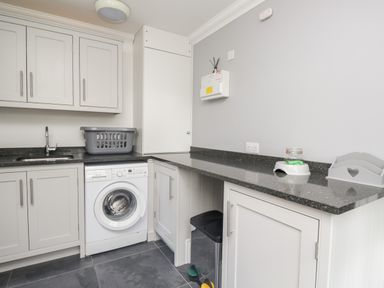A laundry room with a washing machine grey cabinets a countertop a sink and a laundry basket at Mill End in Eamont Bridge near Penrith