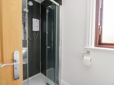 A bathroom with a shower cubicle glass doors a wooden door and a window with a toilet paper holder on the wall at Mill End in Eamont Bridge near Penrith