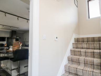 A staircase with plaid carpet next to a kitchen with a black countertop and bar stools at Mill End in Eamont Bridge near Penrith