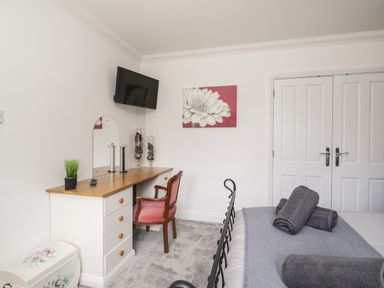 A bedroom with a bed with rolled towels on it a desk with a mirror and chair a wall-mounted tv and double doors at Mill End in Eamont Bridge near Penrith