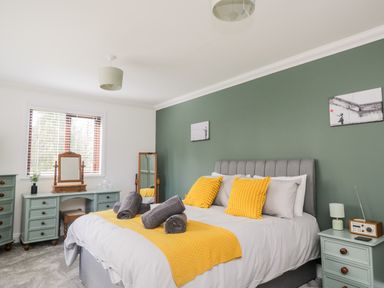A bedroom with a bed yellow pillows and blanket green walls and blue bedside and dressing tables at Mill End in Eamont Bridge near Penrith