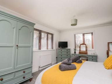 A bedroom with green wardrobes a dresser a television and a bed with yellow bedding at Mill End in Eamont Bridge near Penrith