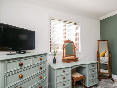 A bedroom corner with a dresser, vanity table with mirror and stool, standing mirror, and a window with blinds at Mill End in Eamont Bridge near Penrith