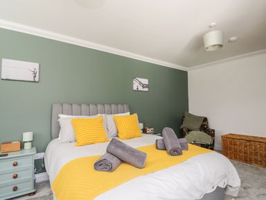 A bedroom with a bed with yellow accents two bedside tables and a chair at Mill End in Eamont Bridge near Penrith