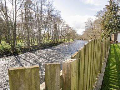 A river with a wooden fence and grass on the right side and trees on the left side at Mill End in Eamont Bridge near Penrith