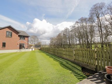 A backyard with a green lawn and a wooden fence next to a brick house at Mill End in Eamont Bridge near Penrith