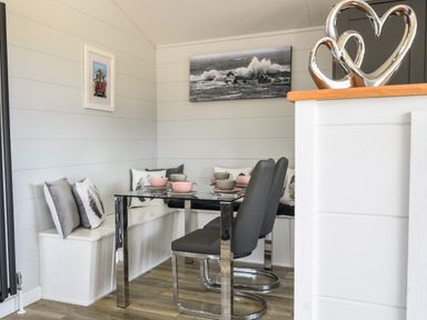 A dining area with a glass table set with bowls and plates black chairs and a built in bench with cushions at Oakwood 2 @ Pinewood Retreat in Pinewood