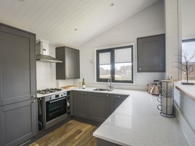 A kitchen with gray cabinets white countertops a gas stove oven and sink at Oakwood 2 @ Pinewood Retreat in Pinewood