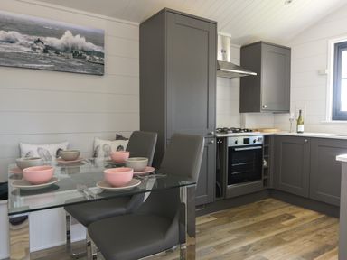 A kitchen with grey cabinets glass dining table with bowls and chairs at Oakwood 2 @ Pinewood Retreat in Pinewood