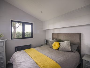 A bedroom with a bed with grey and yellow bedding next to a window at Oakwood 2 @ Pinewood Retreat in Pinewood