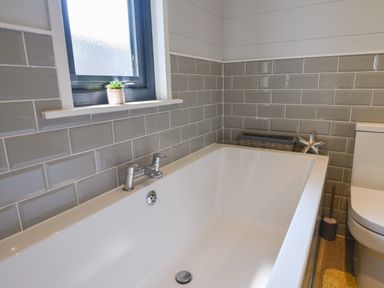 A bathroom with a white bathtub next to a window and toilet at Oakwood 2 @ Pinewood Retreat in Pinewood