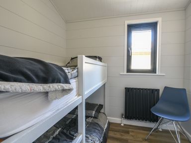 A small bedroom with white bunk beds a blue chair a black radiator and a small window at Oakwood 2 @ Pinewood Retreat in Pinewood