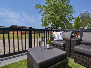 An outdoor seating area with wicker chairs and a table with a bottle of wine and two glasses at Oakwood 2 Pinewood Retreat Pinewood