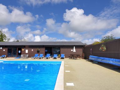 An outdoor swimming pool with blue lounge chairs and a brown wooden building at Oakwood 2 @ Pinewood Retreat in Pinewood