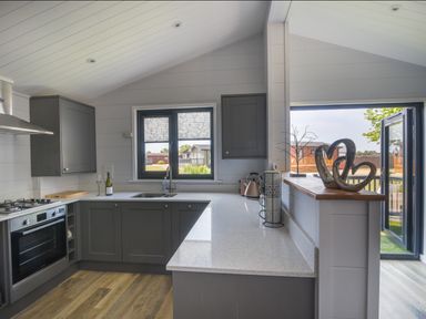 A kitchen with dark cabinets a countertop a sink stove and oven with a window and open doors at Oakwood 2 @ Pinewood Retreat in Pinewood