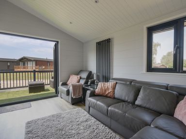 A living room with gray leather sofas, a gray armchair, a side table with a lamp, a rug, and an open door leading to a patio at Oakwood 2 @ Pinewood Retreat in Pinewood