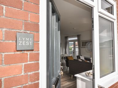 An open door showing a living room with chairs a table and curtains at Lyme Zest in Lyme Regis