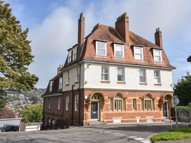A large brick and stucco building with multiple chimneys and black doors on a street corner at Lyme Zest in Lyme Regis