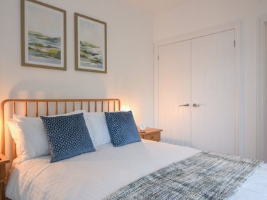 A bedroom with a wooden bed frame blue pillows white bedding two framed landscape paintings on the wall and white double doors at Lyme Zest in Lyme Regis