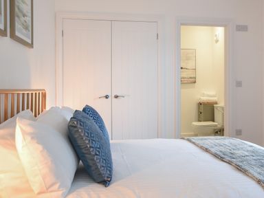 A bedroom with a bed with blue pillows white doors and a bathroom with toilet at Lyme Zest in Lyme Regis