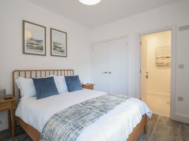 A bedroom with a wooden bed frame blue pillows and a blanket two wooden bedside tables and framed paintings at Lyme Zest Lyme Regis