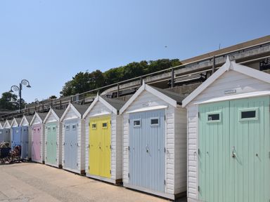 A row of white beach huts with pastel colored doors under a clear sky at Lyme Zest in Lyme Regis