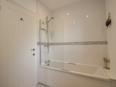 A bathroom with a bathtub and shower with glass screen and a closed white door at Lyme Zest in Lyme Regis