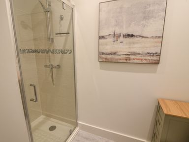 A bathroom with a glass shower enclosure a tiled shower with a mosaic strip a painting on the wall and a green wooden cabinet with a wooden top at Lyme Zest in Lyme Regis