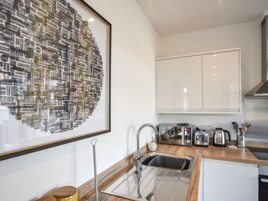 A kitchen with a sink toaster kettle microwave white cabinets and artwork on the wall at Lyme Zest in Lyme Regis