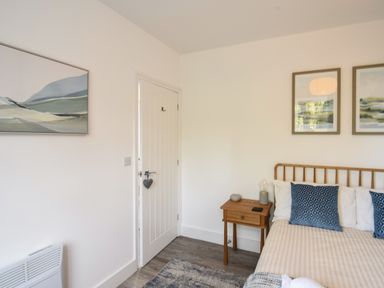 A bedroom with a bed a wooden bedside table two framed pictures on the wall and a closed door at Lyme Zest in Lyme Regis