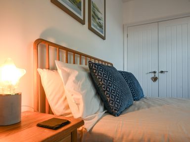 A bedroom with a wooden bed frame blue pillows white pillows a wooden nightstand with a lamp and two framed pictures above the bed at Lyme Zest in Lyme Regis
