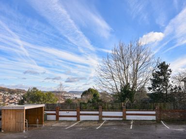 A parking area with marked spaces a wooden shelter and trees behind a brick and wooden fence at Lyme Zest in Lyme Regis