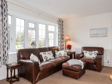 A sitting room with brown leather sofas a lamp and a window with patterned curtains at Neaudd Wen Red Wharf Bay near Benllech