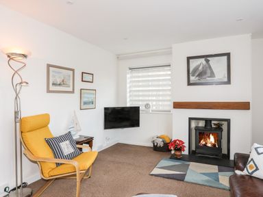 A living room with a yellow armchair a fireplace a TV and framed pictures on the wall at Neaudd Wen in Red Wharf Bay near Benllech