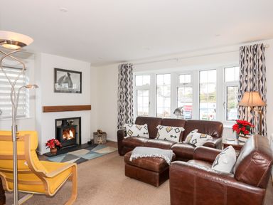 A living room with leather sofas a yellow armchair a fireplace and patterned curtains at Neaudd Wen in Red Wharf Bay near Benllech