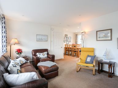 A living room with leather sofa and armchair a yellow chair and dining table with chairs at Neaudd Wen in Red Wharf Bay near Benllech