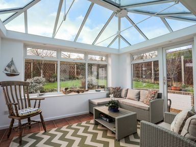 A conservatory with glass ceiling a sofa armchair wooden chair and coffee table with garden view at Neaudd Wen Red Wharf Bay near Benllech
