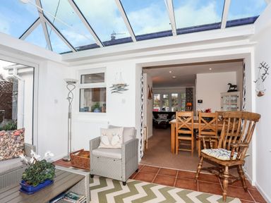 A sunroom with wicker chairs and a wooden chair next to a dining room with wooden table and chairs at Neaudd Wen Red Wharf Bay near Benllech