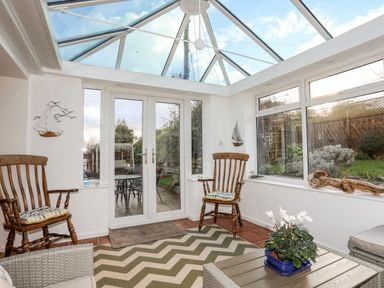 A sunroom with wooden chairs a coffee table with a plant a zigzag rug and double glass doors at Neaudd Wen Red Wharf Bay near Benllech