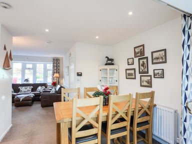 A dining area with wooden table and chairs next to a living room with brown leather sofas at Neaudd Wen Red Wharf Bay near Benllech
