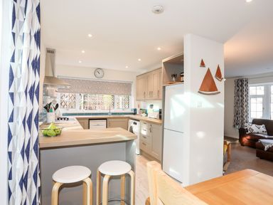 A kitchen with wooden countertops stools a refrigerator and a living room with a sofa in the background at Neaudd Wen in Red Wharf Bay near Benllech