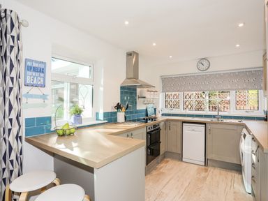 A kitchen with wooden countertops blue tile backsplash and grey cabinets with stools at Neaudd Wen in Red Wharf Bay near Benllech