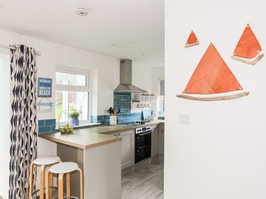 A kitchen with stools at a counter and orange sailboat decorations on the wall at Neaudd Wen in Red Wharf Bay near Benllech