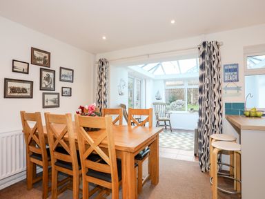 A dining room with wooden chairs and a table next to a sunroom with rocking chairs and patterned curtains at Neaudd Wen Red Wharf Bay near Benllech