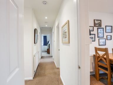 A hallway with carpet and framed pictures on the walls leading to a room with a window Neaudd Wen Red Wharf Bay near Benllech