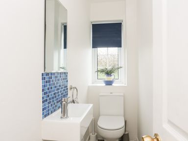 A bathroom with a toilet a small sink with blue tiles and a window with a blue blind and a plant on the windowsill at Neaudd Wen in Red Wharf Bay near Benllech