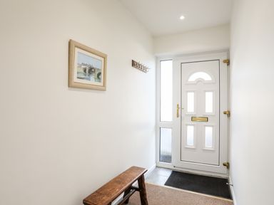 An entryway with a white front door a wooden bench a coat rack and a framed picture on the wall at Neaudd Wen in Red Wharf Bay near Benllech