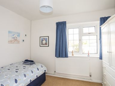 A bedroom with a single bed with seagull bedspread blue curtains window and white wardrobe at Neaudd Wen in Red Wharf Bay near Benllech