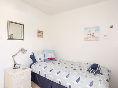 A bedroom with a single bed with seagull printed bedding a bedside table with a lamp and framed pictures on the walls at Neaudd Wen Red Wharf Bay near Benllech